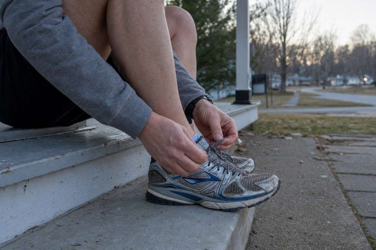 Close view of a runner lacing up shoes on a porch step